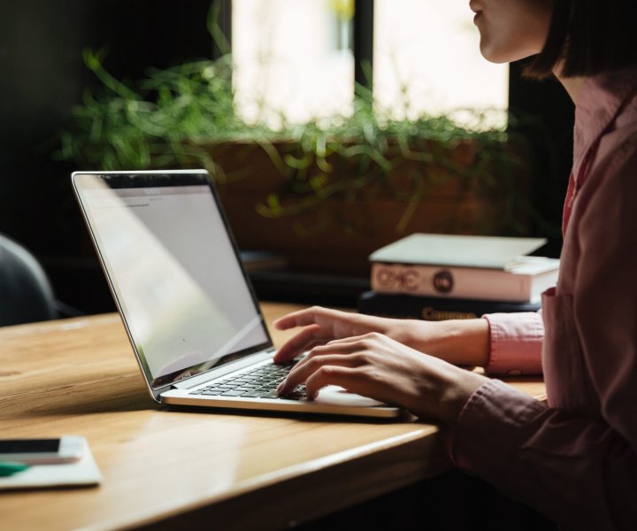 Cropped Side view of brunette woman sitting by the table in cafe and using laptop computer