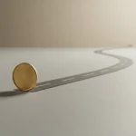 Unmarked brass coin on a clean desk with a single path extending into a soft horizon, symbolizing a first paid step shaping a career.