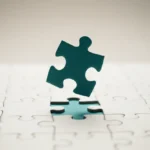 Teal puzzle piece aligned above its matching slot on a white puzzle, symbolizing a small test before broader delegation.